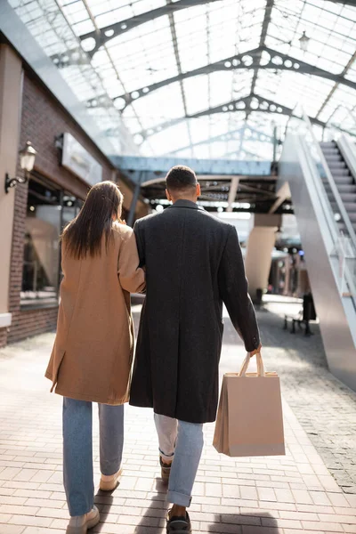 back view of african american man with shopping bags walking with brunette girlfriend on urban street