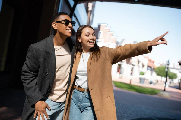 Excited Woman Coat Looking Away Pointing Finger African American Man — Stock Photo, Image
