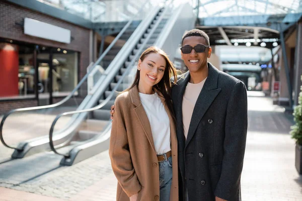 Trendy Interracial Couple Coats Smiling Camera Blurred Escalator Street — Stock Photo, Image