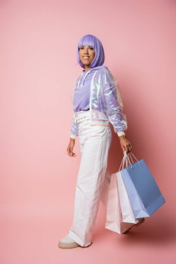 Tam boy, şeffaf ceketli, pembe çantalı, neşeli Afro-Amerikalı kadın. 