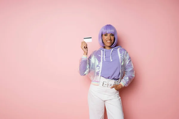 幸せなアフリカ系アメリカ人女性で紫の髪クレジットカードを保持し ピンクのポケットに手でポーズ — ストック写真