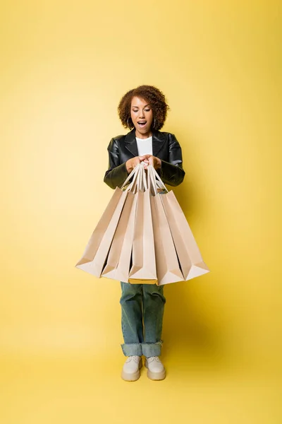Aufgeregte Afroamerikanerin Stylischer Lederjacke Mit Einkaufstaschen Mit Einkäufen Auf Gelb — Stockfoto