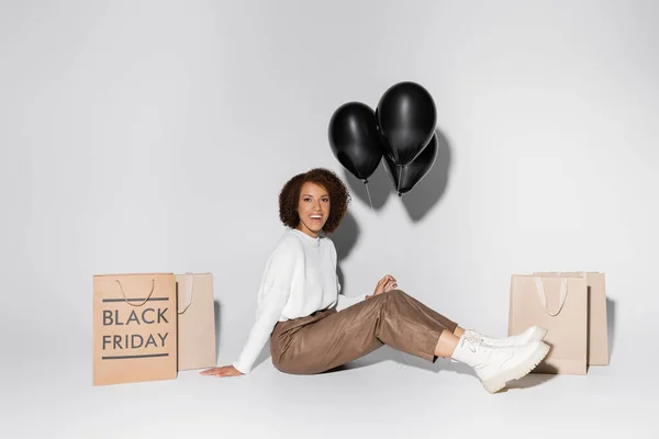 Alegre Mujer Afroamericana Traje Otoñal Sosteniendo Globos Negros Cerca Bolsas —  Fotos de Stock