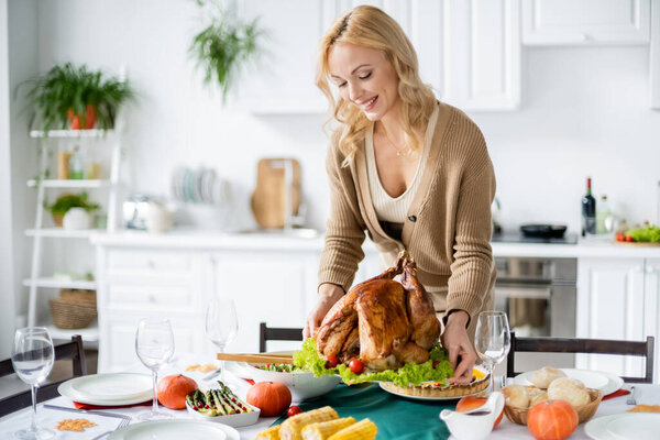Smiling woman putting thanksgiving turkey on table at home 