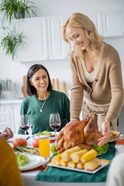 Madre Multicultural Sentada Cerca Hija Poniendo Pavo Festivo Mesa Casa —  Fotos de Stock