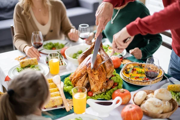 Man Skär Kalkon Nära Suddig Familj Och Välsmakande Thanksgiving Middag — Stockfoto