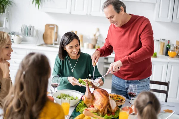 Alegre Abuelo Poniendo Pavo Plato Cerca Mujeres Niños Multiculturales Durante — Foto de Stock