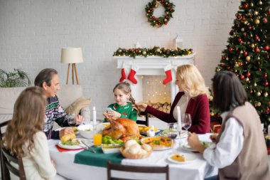 Çok ırklı bir ailenin yanında, kızının saçına dokunan bir kadın Noel yemeği yiyor.