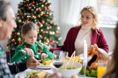 Gülümseyen kadın kızına bakıyor Noel ağacının yanında aile yemeği yiyor.