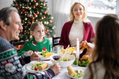 Neşeli bir kadın Noel ağacının yakınındaki şenlikli bir akşam yemeğinde ailesine bakıyor.