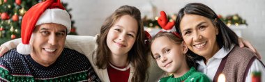 Mutlu kız kardeşler Noel 'i ve pankartı kutlarken ırklar arası büyükanne ve büyükbabaların yanında kameraya bakıyor.