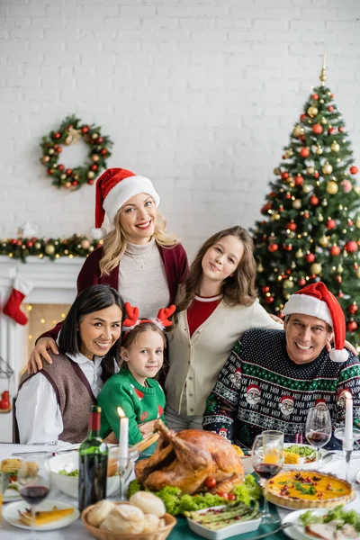 Glad Multietnisk Familj Tittar Kameran Nära Festlig Middag Och Julgran — Stockfoto