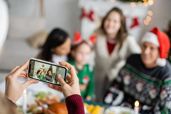 Kobieta Smartfonem Robiącym Zdjęcia Rozmytej Międzyrasowej Rodziny Świętującej Boże Narodzenie — Zdjęcie stockowe