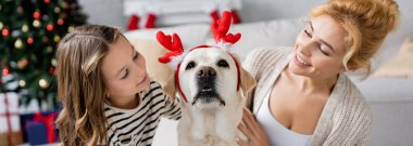 Olumlu kadın ve çocuk evde labrador 'u okşuyor. Yılbaşı bandı takıyor. 