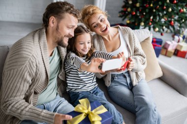 Gülümseyen kız akıllı telefondan aile yanında fincanı ve Noel hediyesiyle selfie çekiyor. 