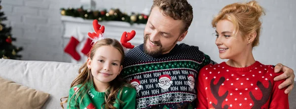 Uśmiechnięci Rodzice Swetrach Patrzący Córkę Świąteczną Opaską Baner — Zdjęcie stockowe