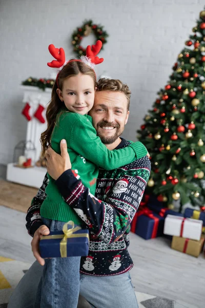 Uśmiechnięty Ojciec Przytulający Córkę Trzymający Prezent Świąteczny Domu — Zdjęcie stockowe