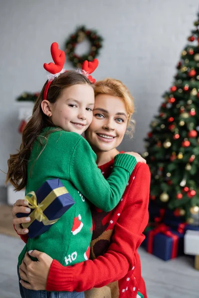 Sonriente Niño Abrazando Madre Suéter Con Celebración Navidad Presente Casa — Foto de Stock