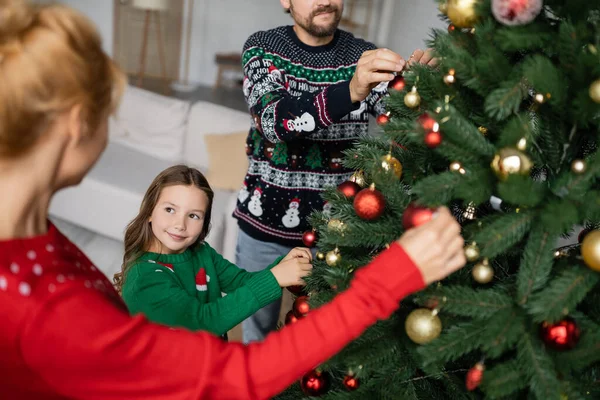 家で両親と一緒にクリスマスツリーを飾るセーターの笑顔の子供 — ストック写真