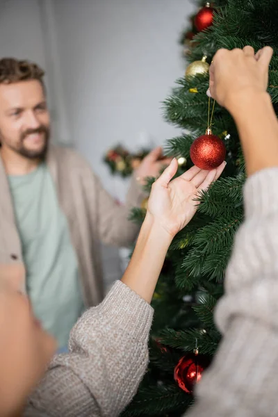 Mulher Segurando Bugigangas Natal Perto Árvore Marido Borrado Casa — Fotografia de Stock