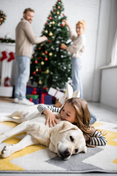 Chica Sonriente Abrazando Labrador Cerca Padres Arrugados Árbol Navidad Casa — Foto de Stock