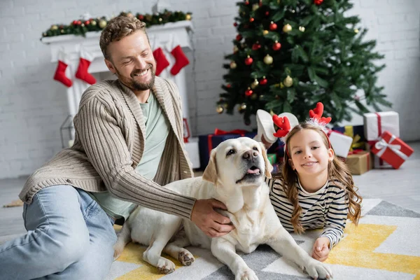 幸せな男Peting Labraador近くにこにこ娘でクリスマスの間にリビングルーム — ストック写真