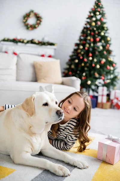 Młoda Dziewczyna Pieszczoty Labrador Pobliżu Boże Narodzenie Prezent Dywanie Domu — Zdjęcie stockowe