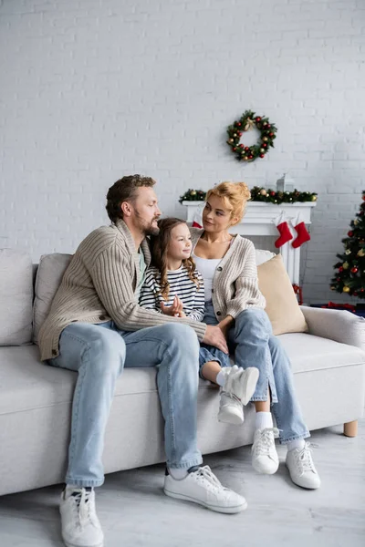 Sonrientes Padres Abrazando Hija Sofá Cerca Decoración Borrosa Navidad Casa — Foto de Stock