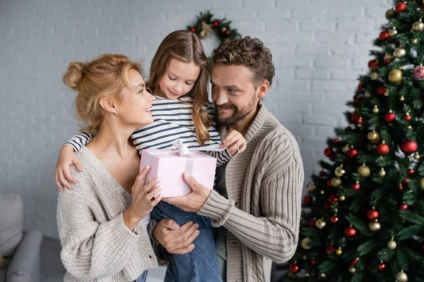 Leende Man Håller Gåva Och Dotter Nära Fru Och Julgran — Stockfoto