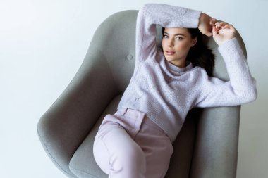 Moda giysiler içinde, beyaz arka planda koltukta dinlenen şehvetli esmer kadın manzarası.