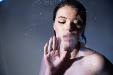 Young woman with naked shoulders looking at wet glass on grey background  clipart