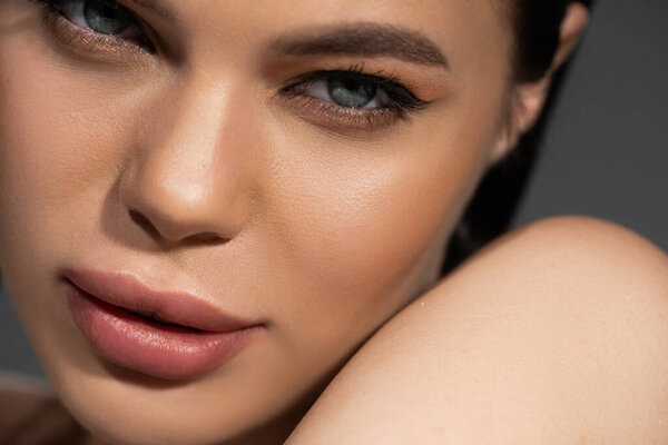 Закрытый вид молодой женщины с проницательным взглядом на камеру у плеча, изолированной на сером фоне 