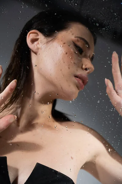 浅见模糊的黑发女子在灰色背景下触摸湿玻璃杯 — 图库照片