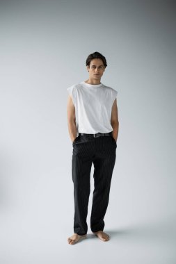 Gri arkaplanda poz veren çıplak ayaklı bir adam. 