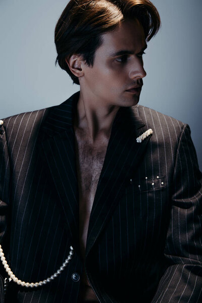 stylish man with hairy chest and trendy suit with pearls looking away on dark gray 