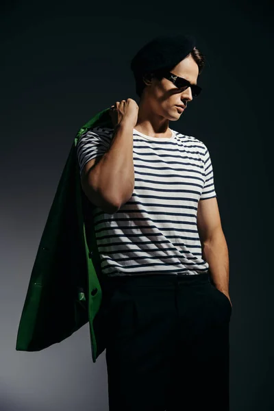 トレンディ男でストライプTシャツ保持グリーンレザージャケット上グレーの背景と照明 — ストック写真