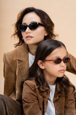 Güneş gözlüklü ve kahverengi süet ceketli moda anne ve kız bej renkli izole edilmiş.