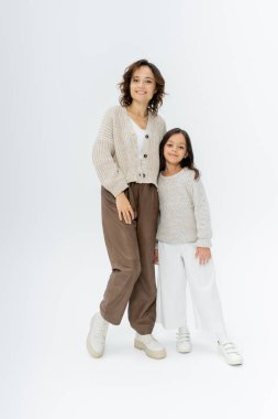 Gri arkaplanda örgü ve pantolon giymiş anne-kız tam boy.