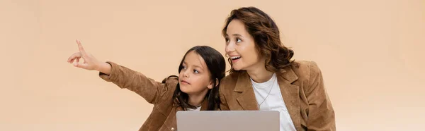 时髦的女孩用手指指尖着笔记本电脑 惊讶的妈妈在米黄色横幅上孤立无援 — 图库照片