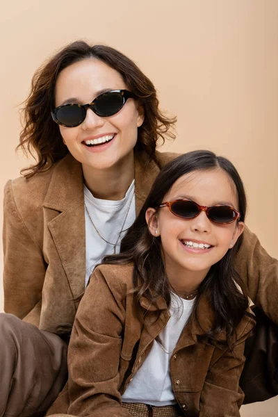 快乐而时尚的母亲和女儿 穿着雪绒服 戴着墨镜 与米色隔离 — 图库照片
