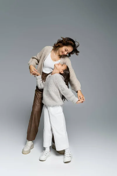 时尚的母亲和女儿手牵着手 面带微笑 同时在灰色的背景下跳舞 — 图库照片