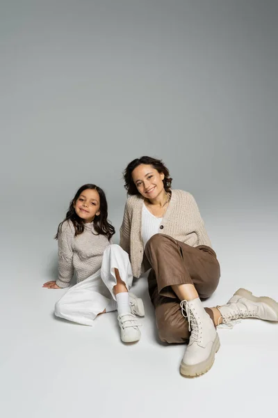 ニットに身を包んだ母親と娘 灰色の背景に座っているパンツ — ストック写真
