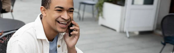 Happy african american man talking on smartphone on summer terrace, banner — Stock Photo