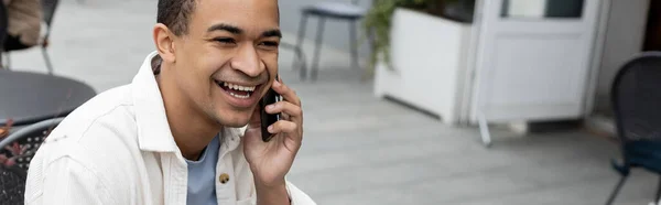 Glücklicher afrikanisch-amerikanischer Mann, der auf der Sommerterrasse mit dem Smartphone spricht, Banner — Stockfoto