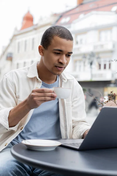 Junge afrikanisch-amerikanische Freiberuflerin mit einer Tasse Kaffee und Laptop auf der Caféterrasse — Stockfoto