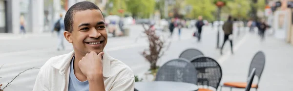 Sonriente hombre afroamericano mirando en la terraza de la cafetería, pancarta - foto de stock