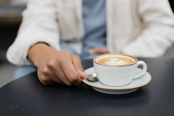 Vista ritagliata dell'uomo africano americano che tiene il piattino con la tazza di cappuccino sulla terrazza estiva — Foto stock