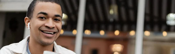 Cheerful african american man in wireless earphones looking at camera, banner — Stock Photo