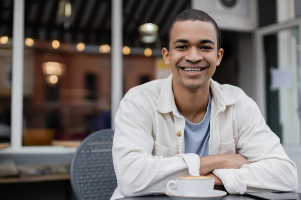 Glücklicher und junger afrikanisch-amerikanischer Mann blickt auf Sommerterrasse in die Kamera — Stockfoto
