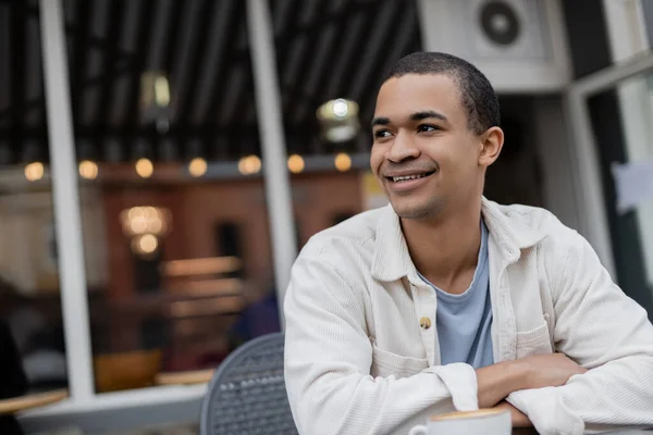 Sonriente y joven hombre afroamericano mirando hacia otro lado en la terraza de verano - foto de stock